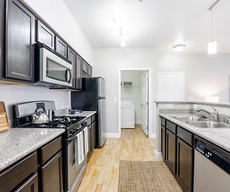 kitchen featuring washer / dryer, gas range oven, stainless steel appliances, dark brown cabinets, light hardwood floors, pendant lighting, and light granite-like countertops, The Trails At Pioneer Meadows