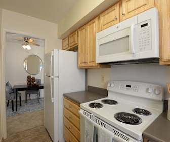 kitchen with a ceiling fan, refrigerator, electric range oven, microwave, light tile floors, dark countertops, pendant lighting, and brown cabinetry, Woodsdale Apartments