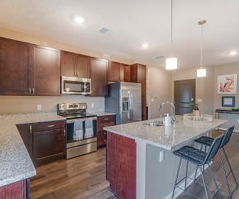 kitchen featuring a kitchen breakfast bar, electric range oven, stainless steel appliances, an island with sink, dark brown cabinetry, pendant lighting, light stone countertops, and light parquet floors, The Flats at Shadow Creek