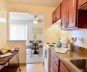 kitchen with natural light, electric range oven, range hood, brown cabinets, light tile flooring, and light stone countertops, Midtown Towers