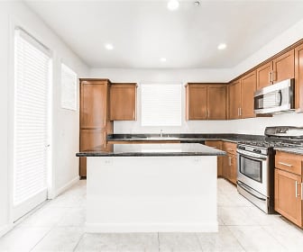 kitchen with a center island, stainless steel microwave, gas range oven, dark stone countertops, light tile flooring, and brown cabinetry, The Croix