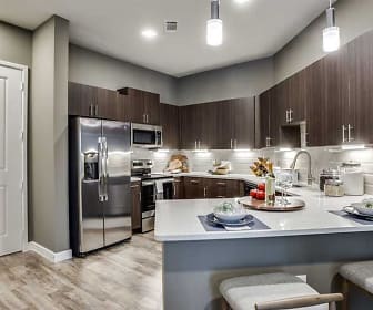 kitchen with a breakfast bar area, stainless steel refrigerator, range oven, microwave, pendant lighting, light flooring, dark brown cabinetry, and light countertops, Junction at Galatyn Park