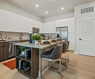 kitchen featuring a kitchen island, a kitchen bar, stainless steel appliances, light hardwood flooring, light stone countertops, and dark brown cabinets, Mirrorton Apartments