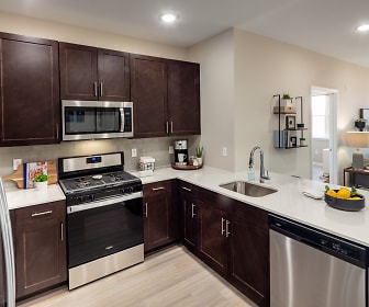 kitchen with gas range oven, stainless steel appliances, dark brown cabinetry, light countertops, and light parquet floors, Lofts at Monroe Parke