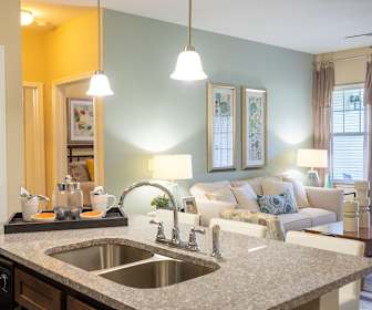 kitchen with a ceiling fan, natural light, dishwasher, light floors, dark brown cabinetry, light granite-like countertops, and pendant lighting, The Legends at White Oak