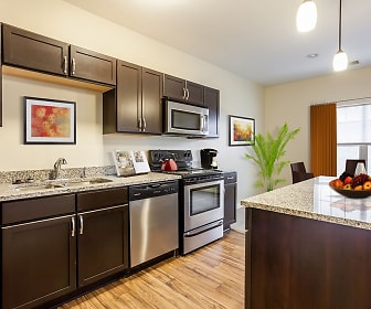 kitchen with a kitchen island, natural light, electric range oven, stainless steel appliances, stone countertops, dark brown cabinets, pendant lighting, and light hardwood flooring, Ethan Pointe Apartments