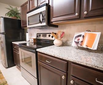 kitchen featuring refrigerator, electric range oven, microwave, light tile floors, stone countertops, and dark brown cabinets, Haven at Commons Park