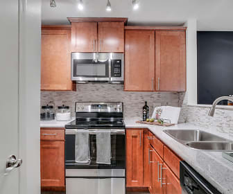 kitchen featuring electric range oven, dishwasher, stainless steel microwave, light granite-like countertops, dark floors, and brown cabinetry, TGM Park Meadows