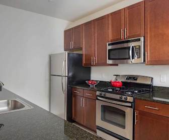 kitchen featuring refrigerator, gas range oven, stainless steel microwave, brown cabinetry, and dark stone countertops, Stone Bridge at Raritan