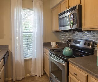 kitchen featuring natural light, dishwasher, electric range oven, stainless steel microwave, dark flooring, dark granite-like countertops, and brown cabinets, Club at North Hills