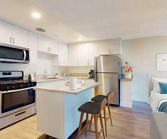 kitchen with a breakfast bar area, stainless steel appliances, gas range oven, white cabinetry, light flooring, and light countertops, Mediterranean Village