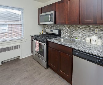 kitchen featuring natural light, stainless steel appliances, radiator, gas range oven, light hardwood flooring, light stone countertops, and dark brown cabinets, Duncan Hill Apartments & Townhomes