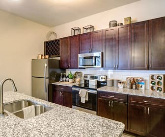 kitchen featuring lofted ceiling, stainless steel microwave, refrigerator, electric range oven, dark brown cabinetry, light granite-like countertops, and kitchen island sink, Brookson Resident Flats
