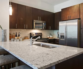 kitchen with a kitchen bar, a center island, electric range oven, stainless steel appliances, light flooring, dark brown cabinetry, pendant lighting, and light stone countertops, Gables University Station