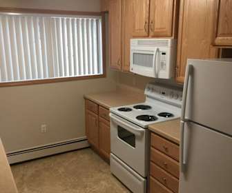 kitchen with a healthy amount of sunlight, refrigerator, electric range oven, baseboard radiator, microwave, light countertops, light tile flooring, and brown cabinetry, Town View Villas