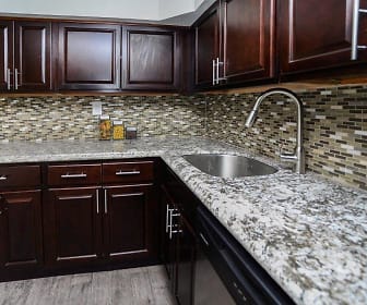 kitchen featuring gas cooktop, dishwasher, microwave, dark brown cabinets, light granite-like countertops, and light hardwood floors, Henry On The Park Apartment Homes