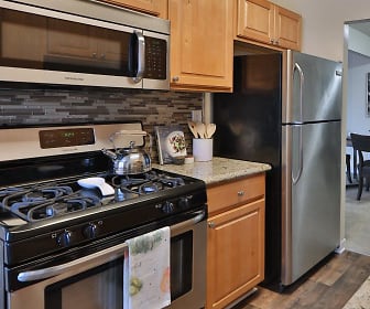 kitchen featuring gas range oven, stainless steel appliances, brown cabinets, light stone countertops, and dark hardwood floors, Chesapeake Glen Apartment Homes